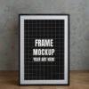 Frame mockup PSD featuring a black and white grid design in a black frame on a wooden surface, accompanied by a textured background.