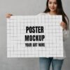 A girl with long hair in a white shirt holding a blank white poster board in front of a gray textured background.