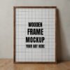 A wooden frame mockup with a blank canvas resting on a wooden table against a textured gray wall.